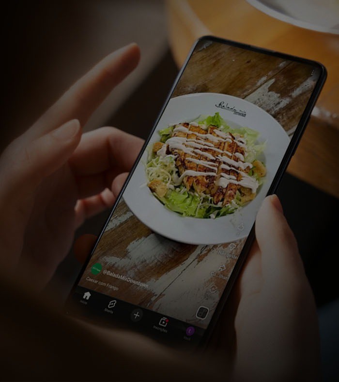 Cliente assistindo ao vídeo de um prato no celular, à mesa do restaurante